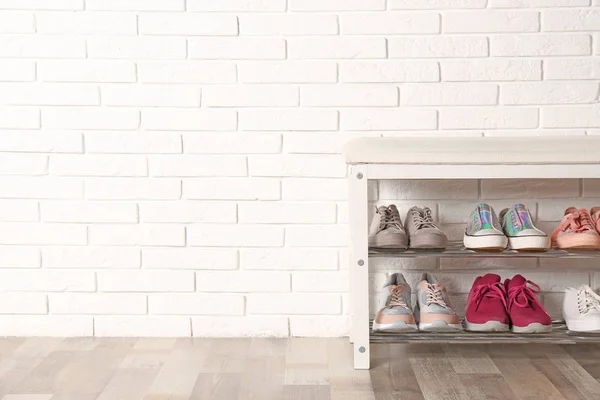 Скамья для хранения обуви с различными кроссовками возле кирпичной стены, место для текста — стоковое фото