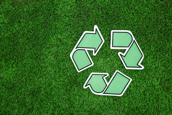 Paper recycling symbol on green grass, top view. Space for text