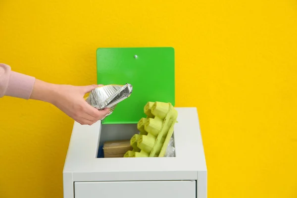 Frau legt gebrauchten Folienbehälter in Mülleimer auf farbigem Hintergrund, Nahaufnahme. Recyclingkonzept — Stockfoto