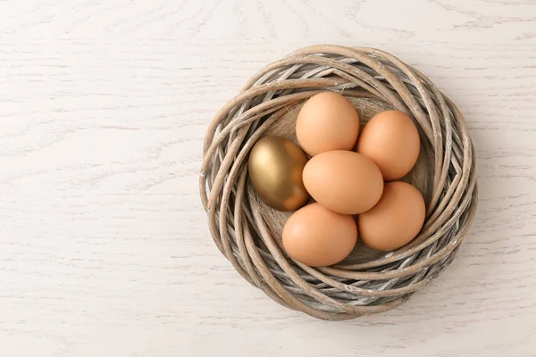 Golden egg among others in nest on wooden background, top view with space for text