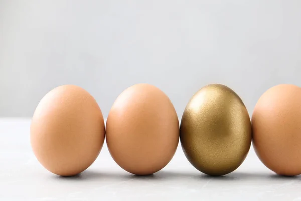Χρυσό αυγό μεταξύ άλλων στο λευκό τραπέζι — Φωτογραφία Αρχείου