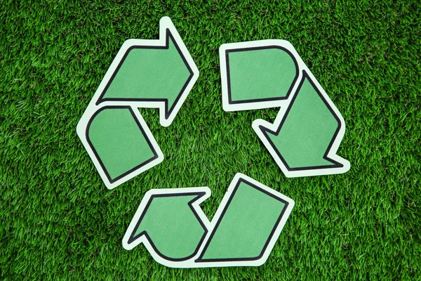 Paper recycling symbol on green grass, top view
