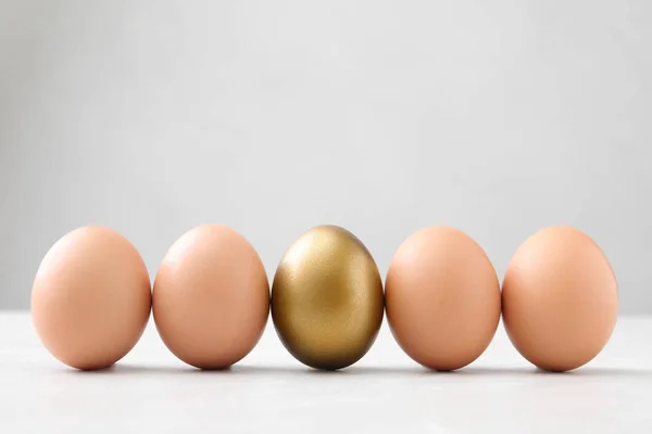 Χρυσό αυγό μεταξύ άλλων στο λευκό τραπέζι — Φωτογραφία Αρχείου