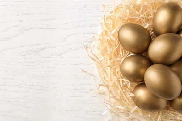 Gouden eieren in het nest op houten achtergrond, bovenaanzicht met ruimte voor tekst — Stockfoto