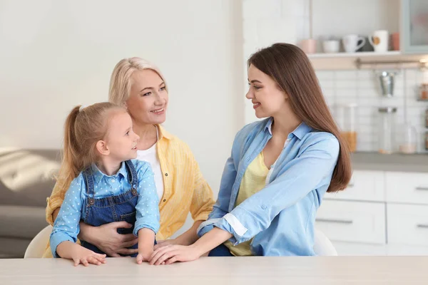 Portrait of young woman with her mother and daughter at table indoors — Stock Photo, Image