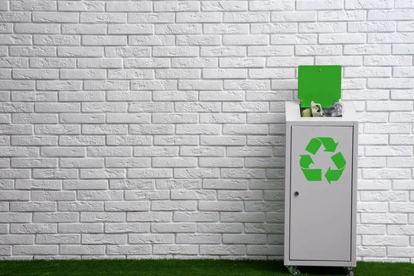 Lixo cheio com símbolo de reciclagem perto da parede de tijolo dentro de casa. Espaço para texto — Fotografia de Stock