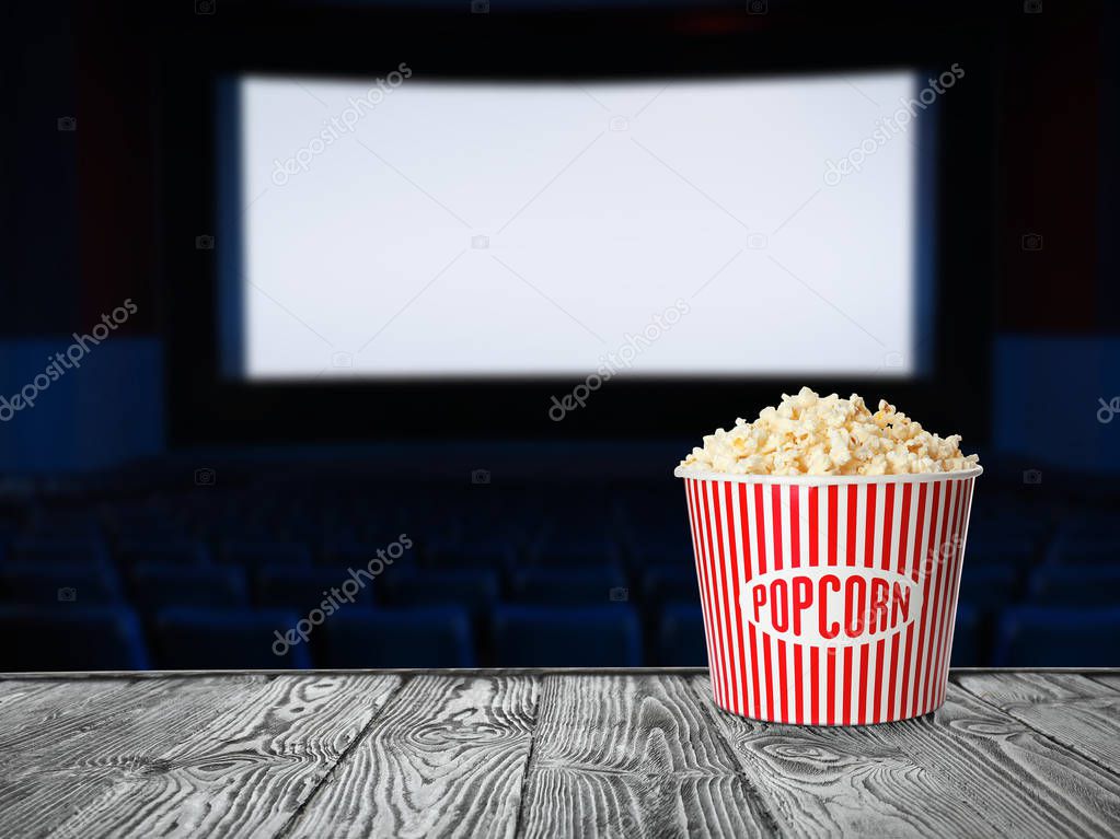 Bucket of popcorn on wooden table in empty cinema hall. Space for text 
