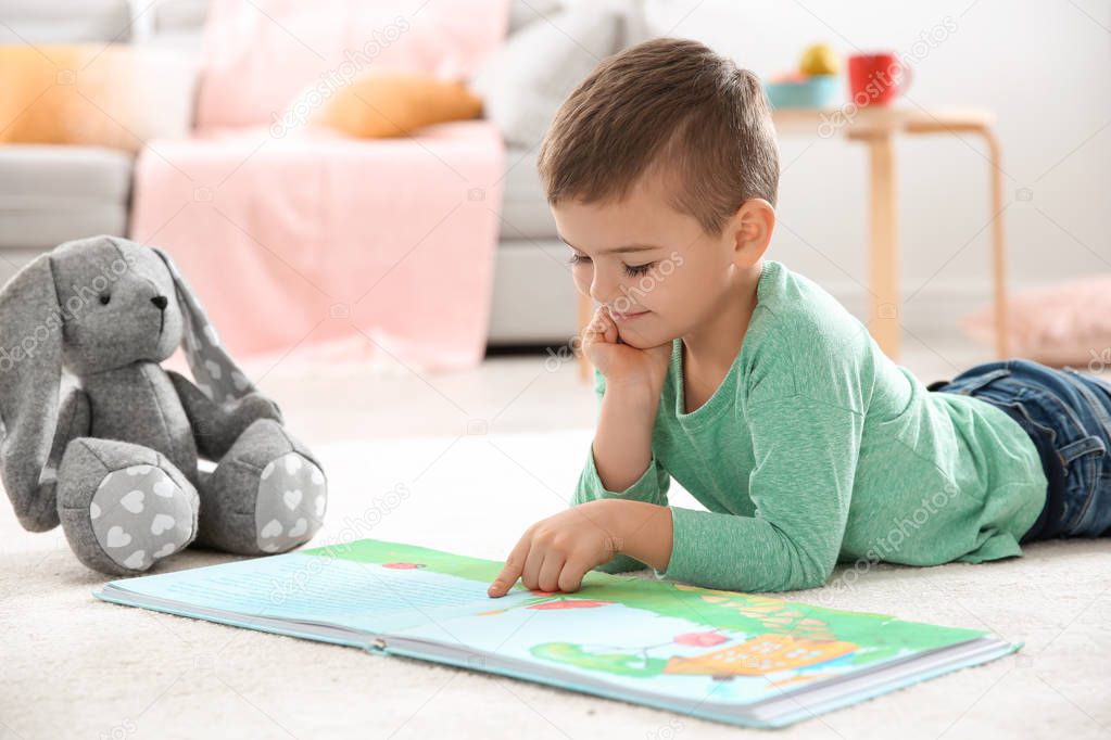 Little boy with toy reading book on floor at home