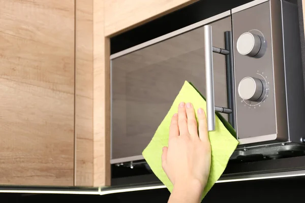 Woman cleaning microwave oven with rag in kitchen, closeup