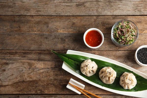 Flat lay composition with plate of tasty baozi dumplings, sesame seeds, sprouts and sauce on wooden table. Space for text — Stock Photo, Image