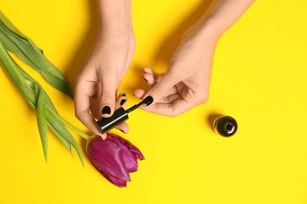 Mujer aplicando esmalte de uñas en flor sobre fondo de color, primer plano — Foto de Stock