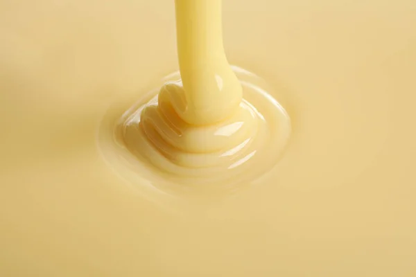 Tasty wlewając mleko skondensowane jako tło, zbliżenie. Produkt Mleczny — Zdjęcie stockowe