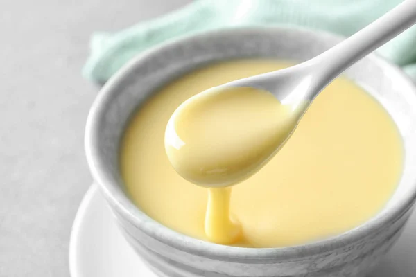 Spoon of pouring condensed milk over bowl on table, closeup. Dairy products — Stock Photo, Image