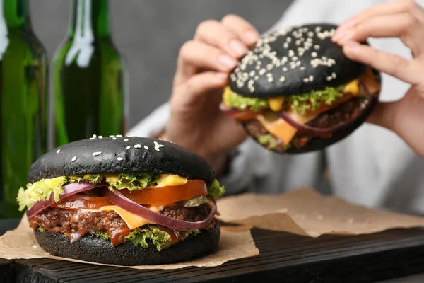 Smakelijke hamburger met zwarte broodjes en vrouw eten op achtergrond — Stockfoto