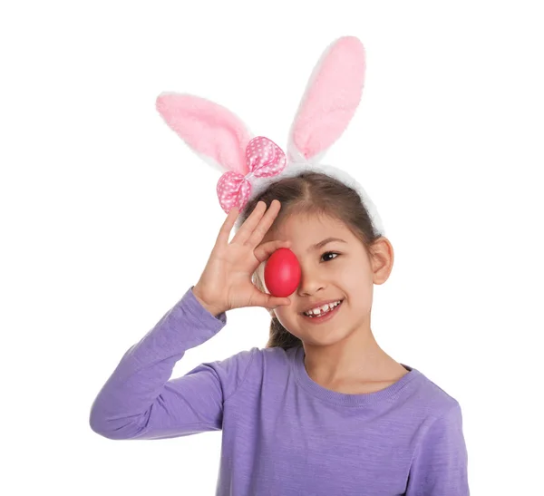 Kleines Mädchen in Hasenohren Stirnband hält Osterei in der Nähe Auge auf weißem Hintergrund — Stockfoto