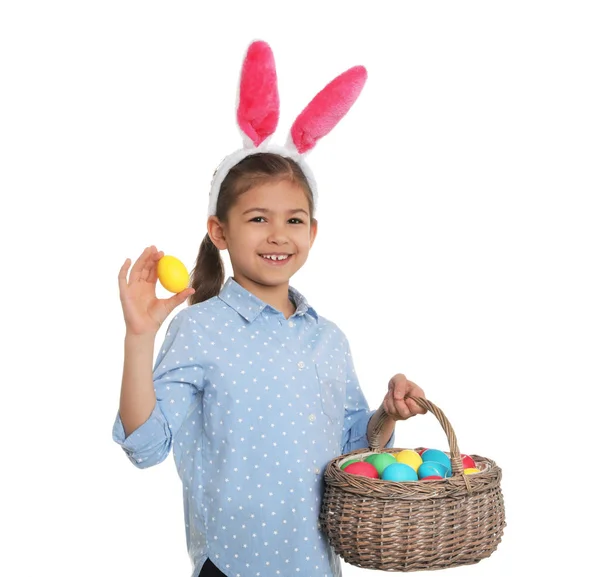 Little girl in bunny ears headband holding basket with Easter eggs on white background — Stock Photo, Image