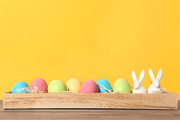 木支架与陶瓷兔子和复活节彩蛋在桌子上反对颜色背景 — 图库照片