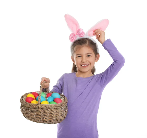 Little girl in bunny ears headband holding basket with Easter eggs on white background — Stock Photo, Image