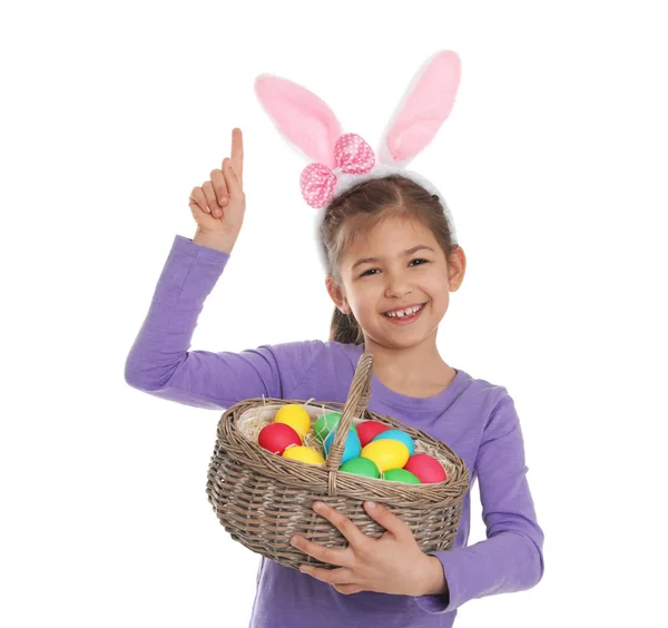 Little girl in bunny ears headband holding basket with Easter eggs on white background — Stock Photo, Image