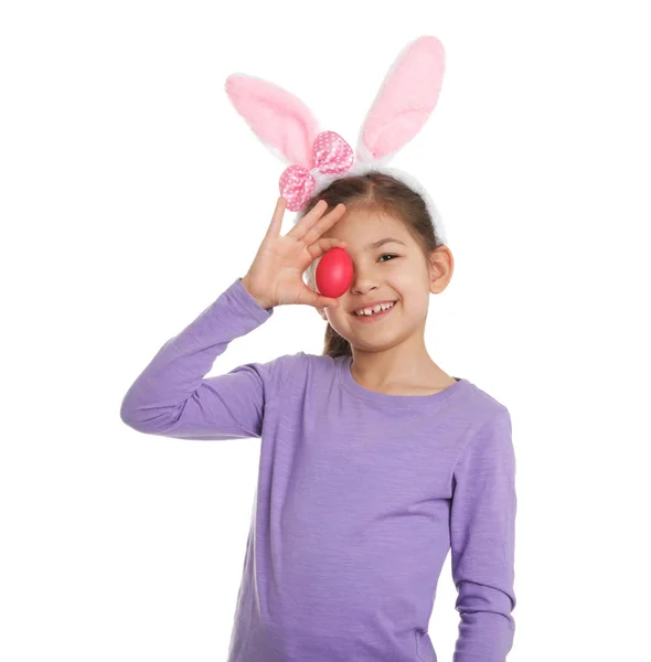 Kleines Mädchen in Hasenohren Stirnband hält Osterei in der Nähe Auge auf weißem Hintergrund — Stockfoto