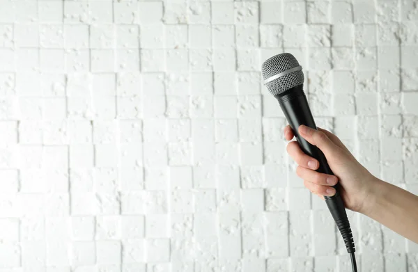 Woman holding modern microphone near white wall, closeup. Space for text — Stock Photo, Image