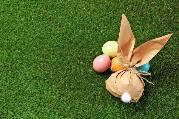 Bolsa de regalo de conejo de Pascua y huevos teñidos en hierba verde, por encima de la vista. Espacio para texto — Foto de Stock