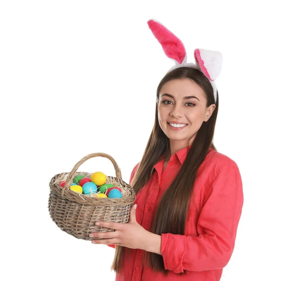 Beautiful woman in bunny ears headband holding basket with Easter eggs on white background — Stock Photo, Image