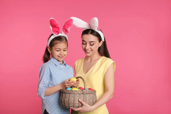 Mother and daughter in bunny ears headbands with Easter eggs on color background — Stock Photo, Image