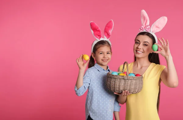 Madre e hija en diademas de orejas de conejo con huevos de Pascua sobre fondo de color, espacio para texto — Foto de Stock