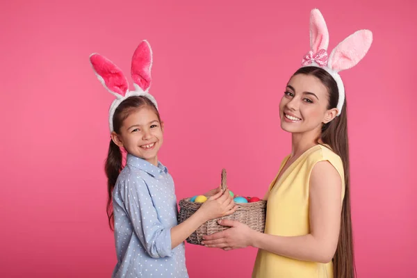 母女俩在兔子耳朵头带拿篮子与复活节彩蛋在颜色背景 — 图库照片