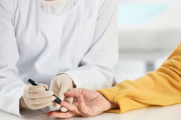 Doctor taking patient's blood sample with lancet pen in hospital, closeup. Diabetes control — Stock Photo, Image