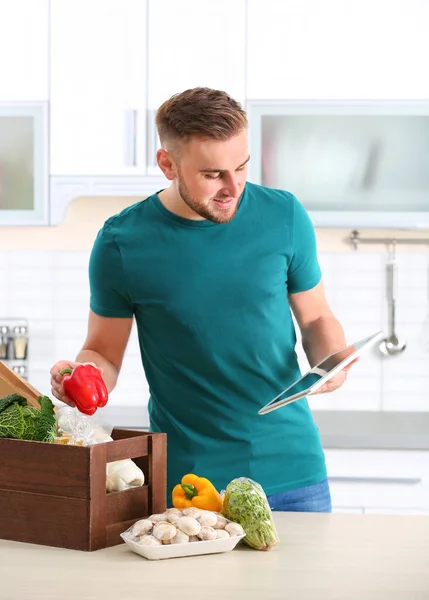 Homme avec caisse en bois pleine de produits et tablette dans la cuisine. Service de livraison de nourriture — Photo