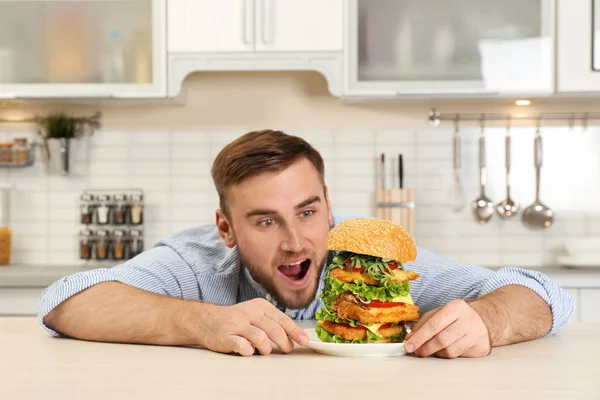 Jovem homem faminto e enorme hambúrguer na mesa — Fotografia de Stock