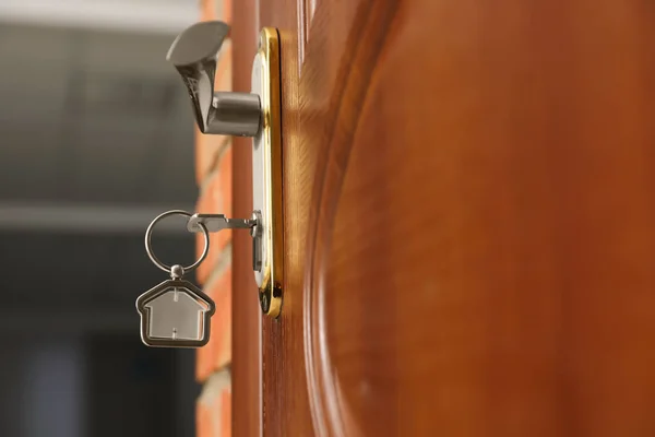 Chave com bugiganga em forma de casa na fechadura da porta, close-up. Espaço para texto — Fotografia de Stock