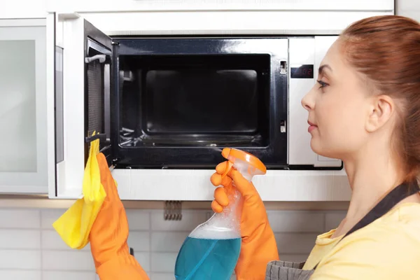 Woman cleaning microwave oven with rag and detergent in kitchen — Stok fotoğraf