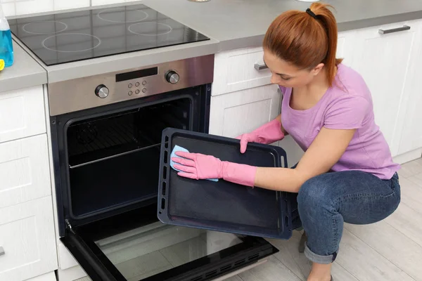 Bandeja de forno de limpeza de mulher com pano na cozinha — Fotografia de Stock