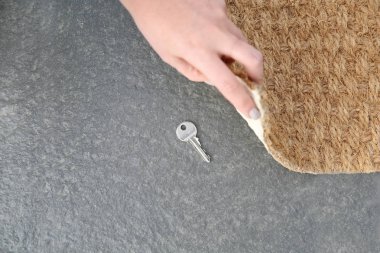 Young woman revealing hidden key under door mat, top view with space for text clipart