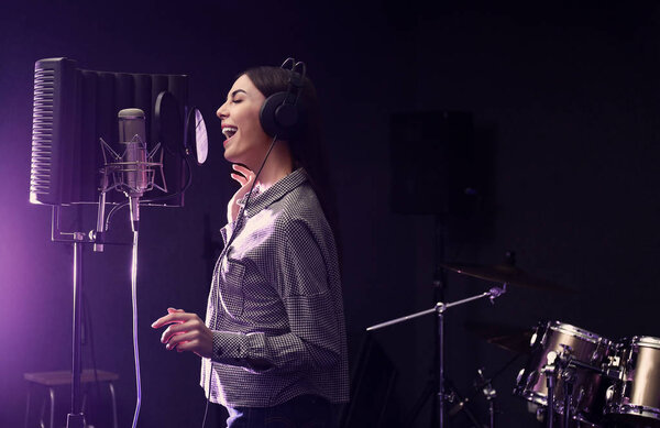 Young singer with microphone recording song in studio. Space for text