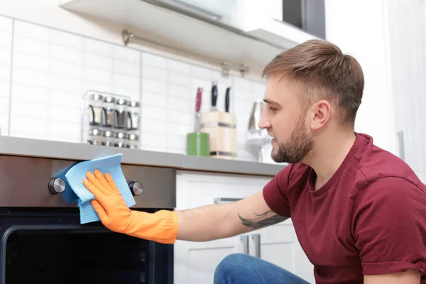 Young man cleaning oven with rag in kitchen — Stock Photo, Image