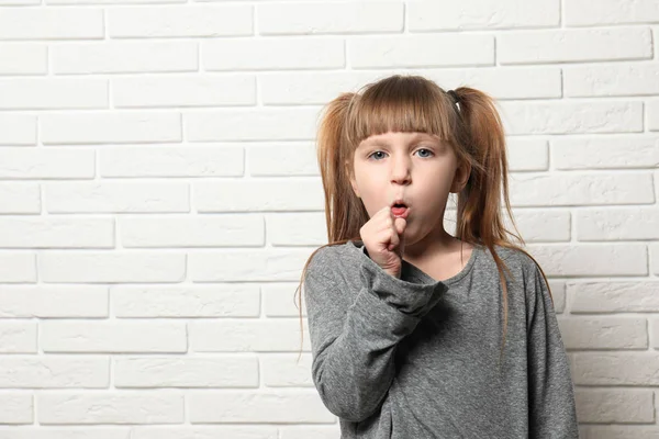 Roztomilá holčička kašle poblíž cihlové zdi. Místo pro text — Stock fotografie