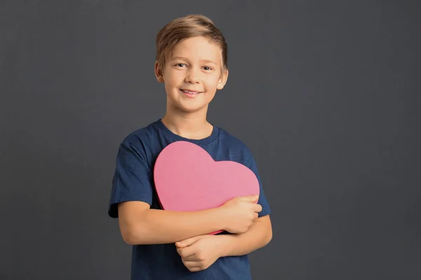 Söt pojke som håller hjärtformad låda på grå bakgrund — Stockfoto