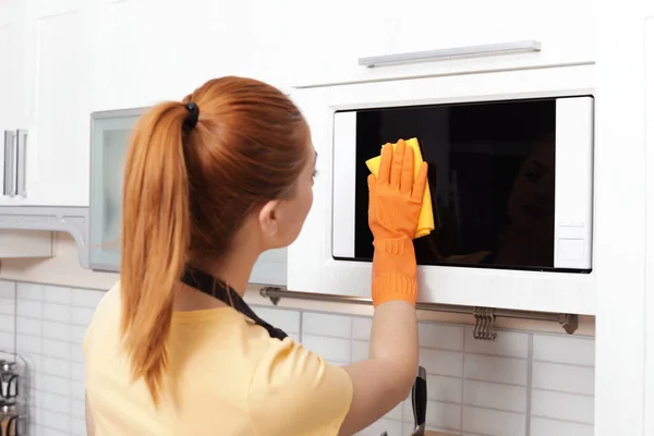 Mulher de limpeza forno de microondas com pano na cozinha — Fotografia de Stock