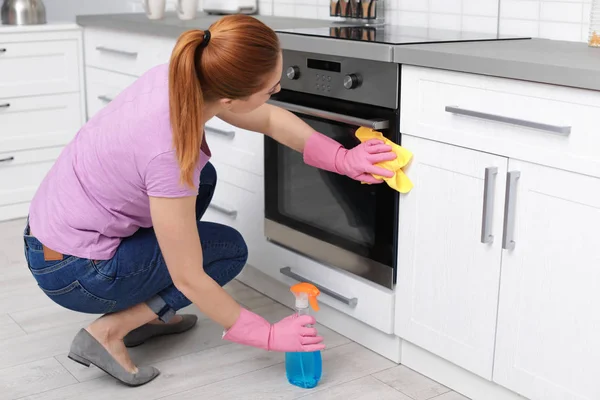 妇女清洁现代烤箱与抹布和洗涤剂在厨房 — 图库照片