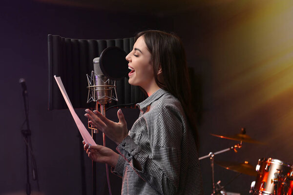 Young singer with microphone recording song in studio