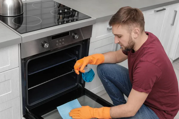 Jovem limpando forno com pano e detergente na cozinha — Fotografia de Stock
