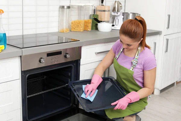 Γυναίκα καθαρισμός δίσκο φούρνου με πανί στην κουζίνα — Φωτογραφία Αρχείου