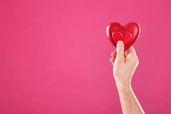 Homem segurando corações decorativos na mão sobre fundo de cor, espaço para texto — Fotografia de Stock