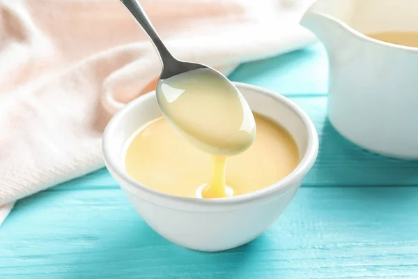 Spoon of pouring condensed milk over bowl on table. Dairy products — Stock Photo, Image