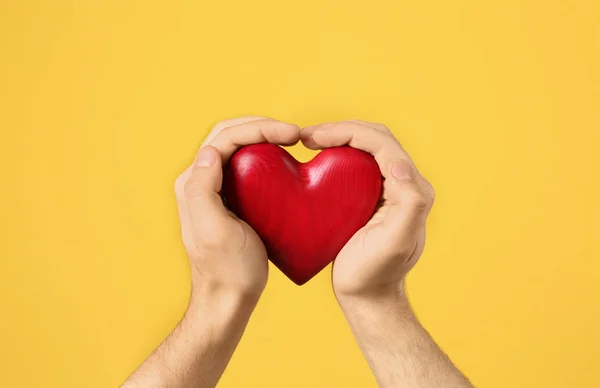 Hombre sosteniendo el corazón decorativo en las manos sobre el fondo de color, primer plano — Foto de Stock