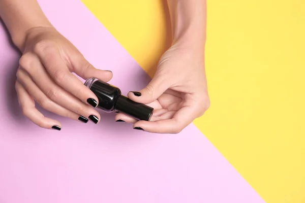 Mujer sosteniendo botella de esmalte de uñas negro sobre fondo de color, primer plano. Espacio para texto — Foto de Stock